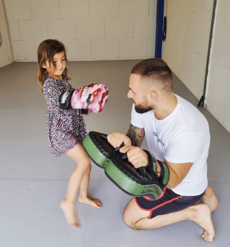 Een kind oefent een trap op een stootkussen dat de trainer vasthoudt bij Fight Ready.
