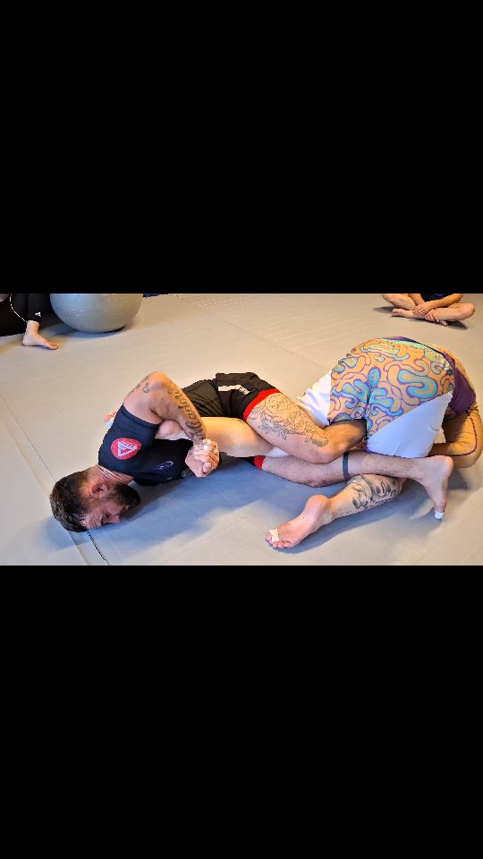 Twee sporters oefenen een beenklem op de mat tijdens een no-gi BJJ-training.