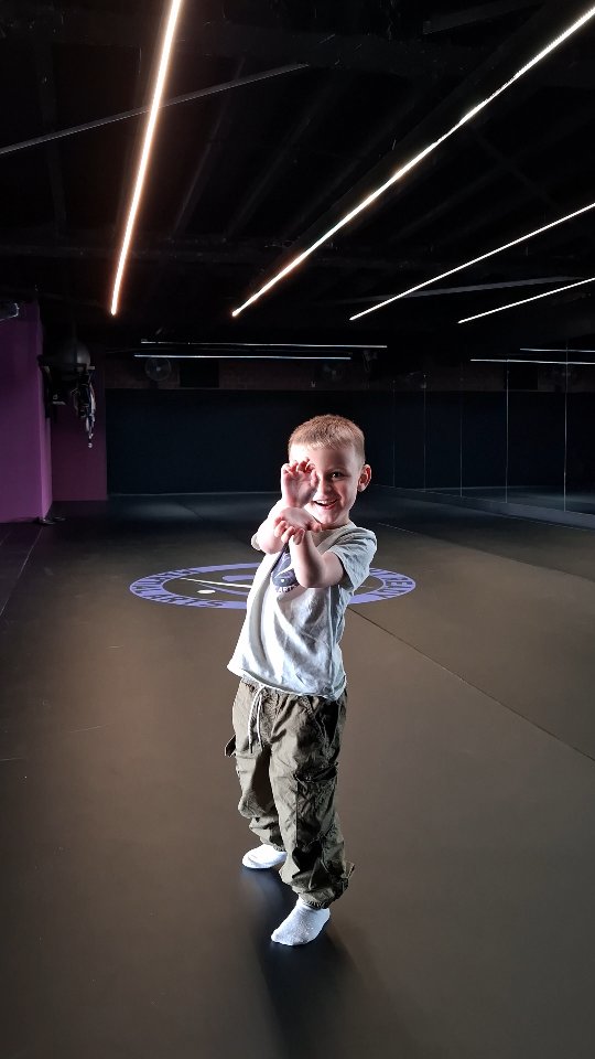 Een lachend kind maakt een speelse houding op de trainingsmat bij Fight Ready.